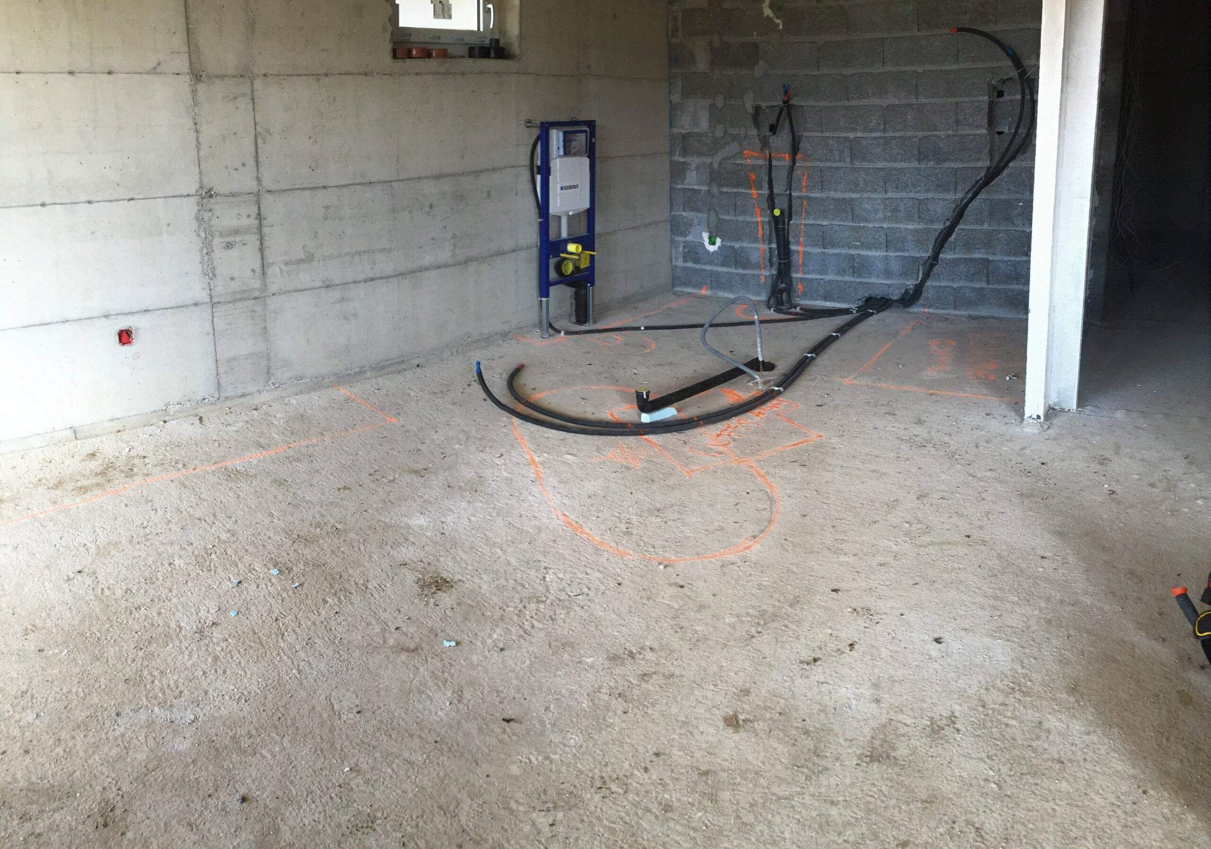 Chantier en cours : bâti-support de WC et alimentations en attente contre un mur en briques