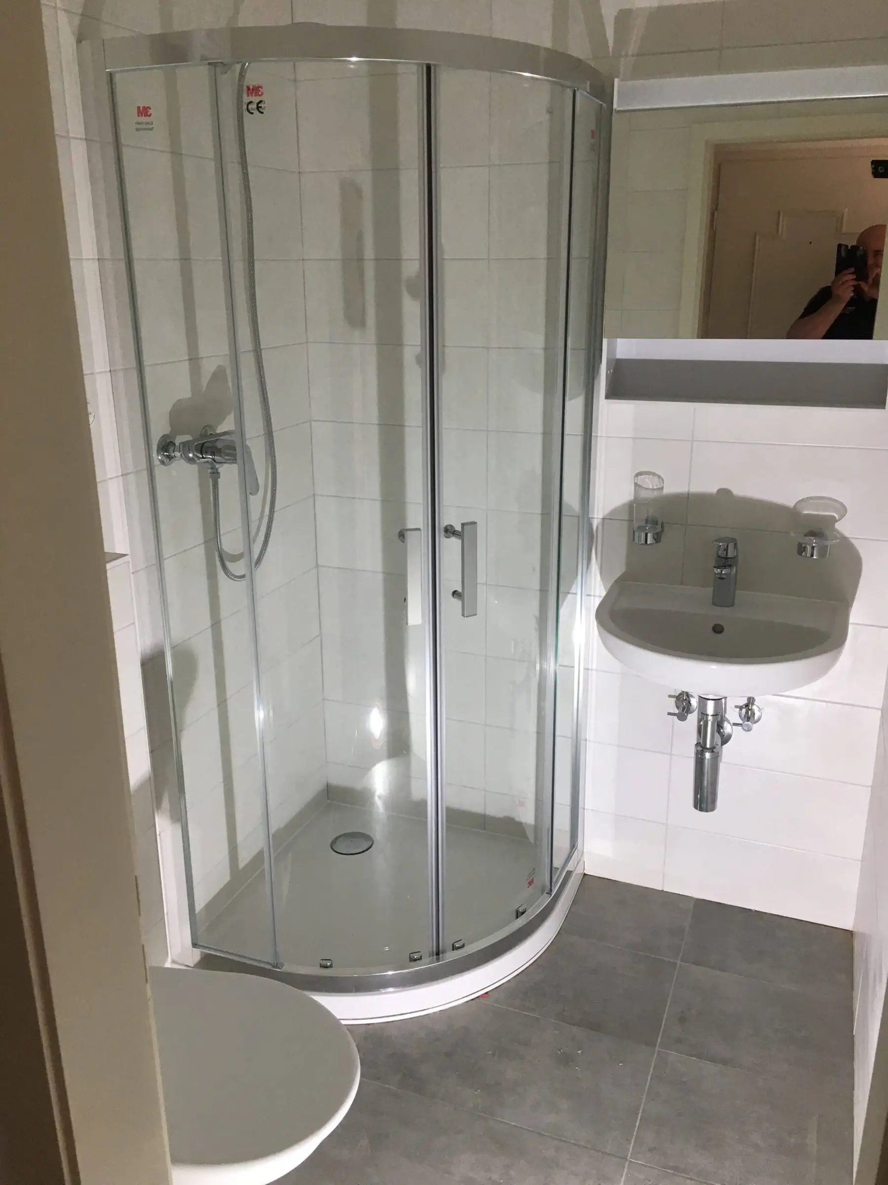 Petite salle d’eau rénovée avec douche d’angle vitrée et lavabo blanc