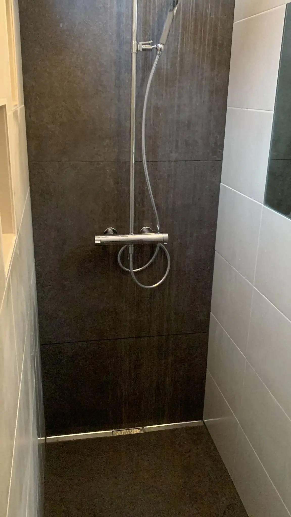 Colonne de douche thermostatique chromée sur un mur en carrelage brun foncé