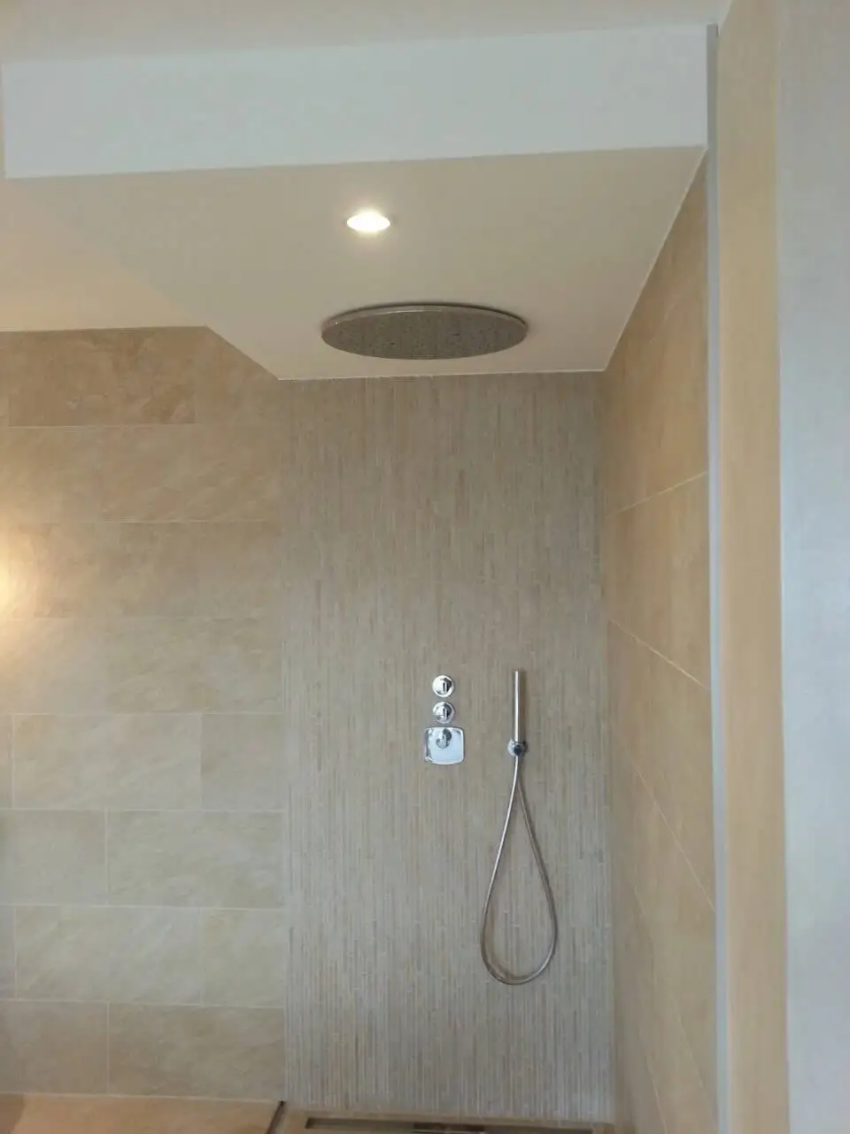 Douche à l’italienne habillée de pierre beige, pomme de douche encastrée au plafond