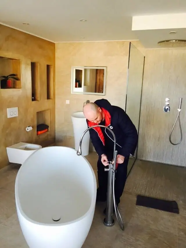 Installateur de Swiss Plomberie réglant un robinet sur colonne à côté d’une baignoire îlot