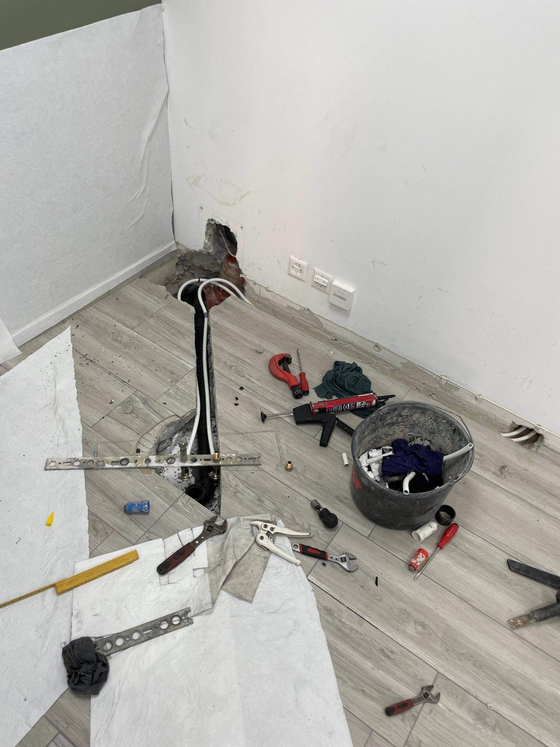 Réparation d’une conduite d’eau sous un plancher ouvert, outils de plombier autour