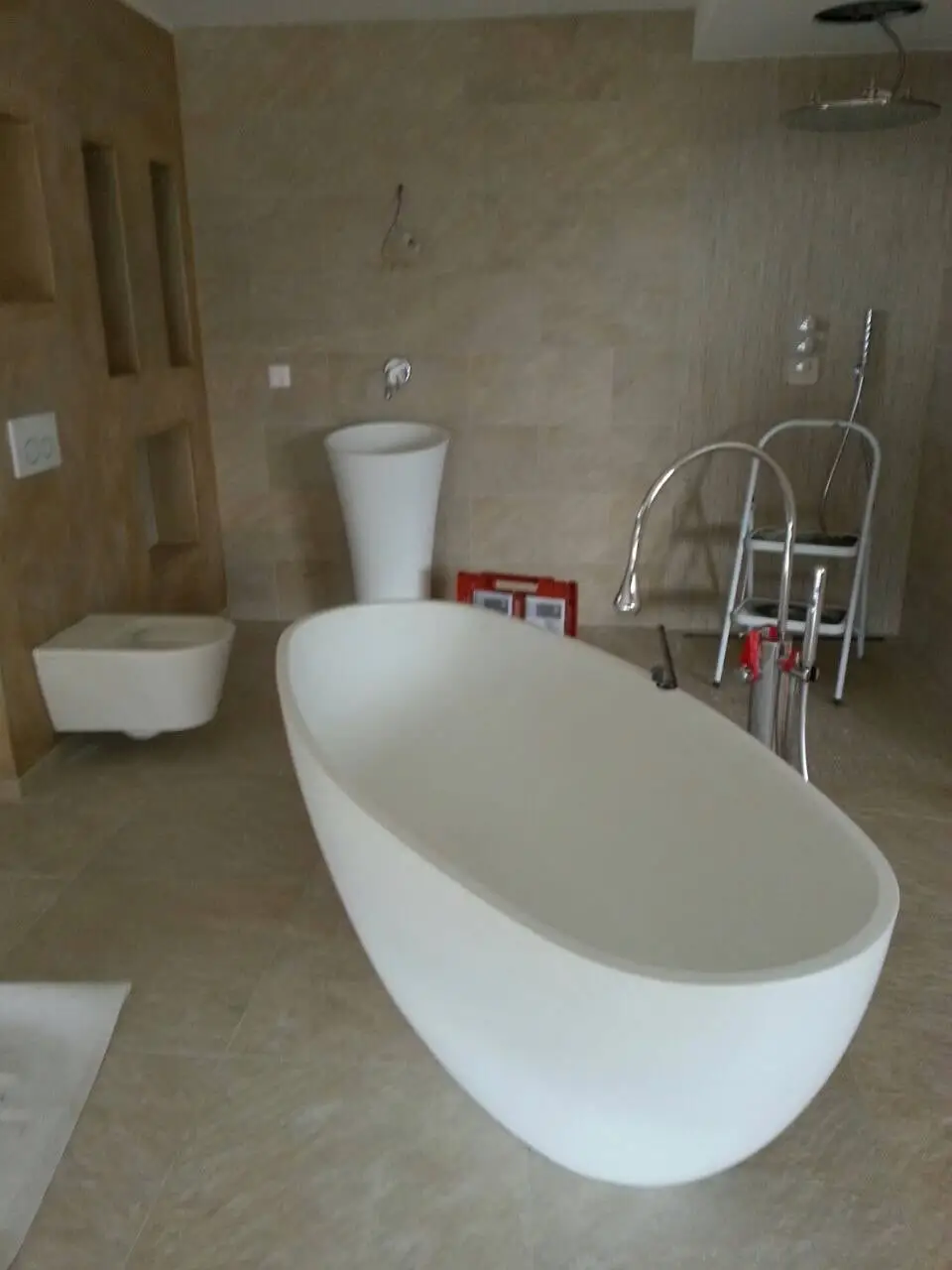 Salle de bain en pierre claire avec baignoire îlot, vasque colonne et WC suspendu