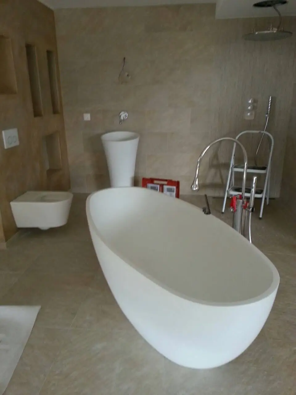 Salle de bain en pierre claire avec baignoire îlot, vasque colonne et WC suspendu
